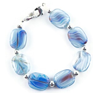 May include: A blue and white glass bead bracelet with silver accents. The beads are oval shaped and have a swirled pattern.