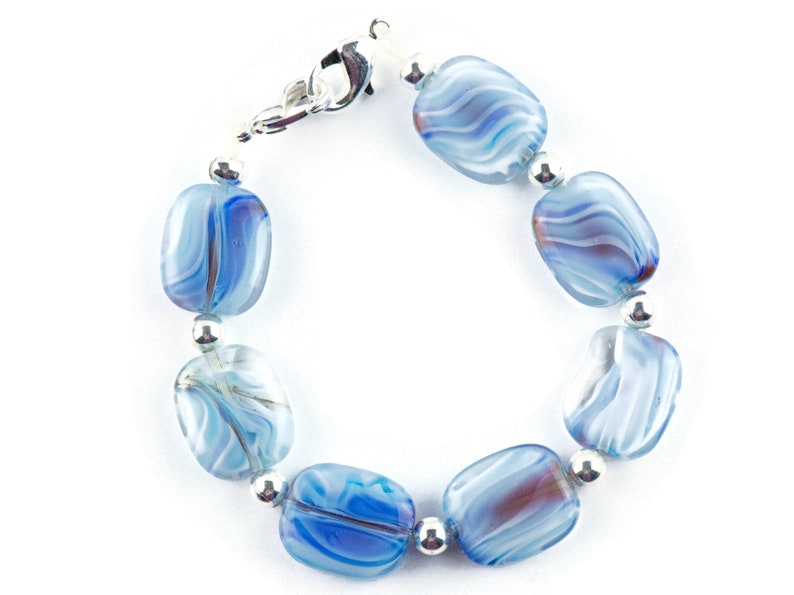 May include: A blue and white glass bead bracelet with silver accents. The beads are oval shaped and have a swirled pattern.