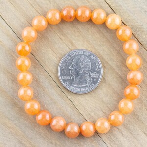 May include: A bracelet made of orange carnelian beads. The bracelet is approximately the size of a US quarter.