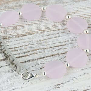 May include: A silver bracelet with a pink glass bead charm and a silver tag engraved with the word "ASTHMA".