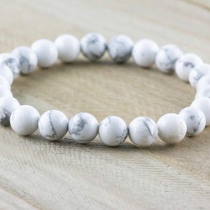 Pode incluir: Pulseira de contas de howlite branca com um design simples. A pulseira &eacute; feita de contas redondas brancas com veios cinzentos subtis.