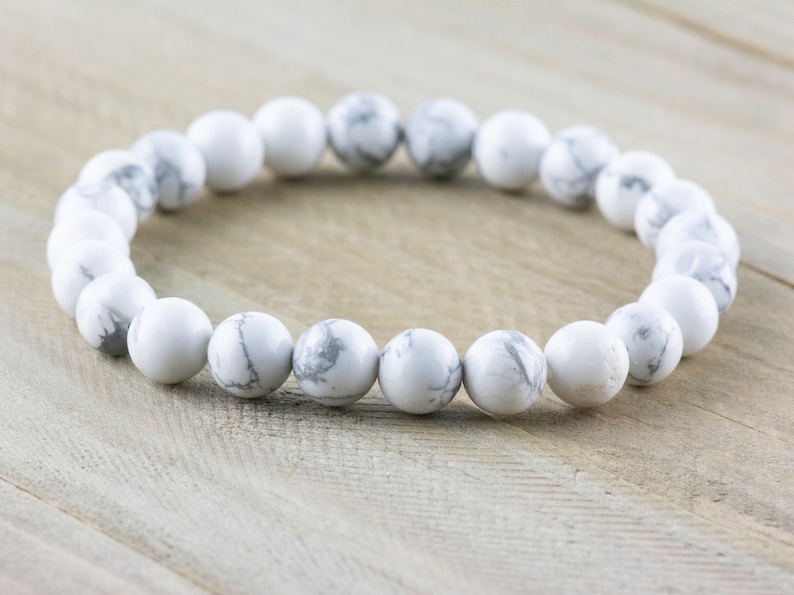 Pode incluir: Pulseira de contas de howlite branca com um design simples. A pulseira &eacute; feita de contas redondas brancas com veios cinzentos subtis.