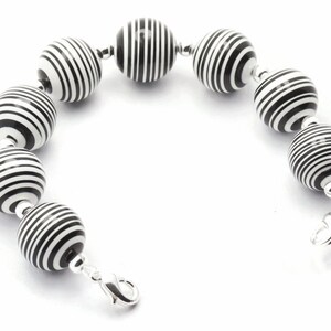 K&ouml;nnte beinhalten: Armband mit schwarzen und wei&szlig;en Streifenperlen und einem silbernen Verschluss.