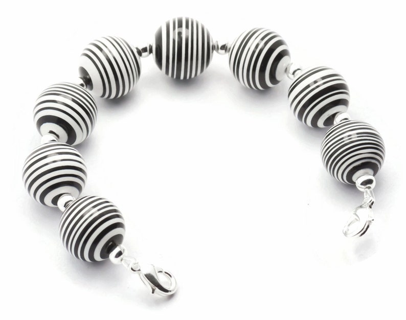 K&ouml;nnte beinhalten: Armband mit schwarzen und wei&szlig;en Streifenperlen und einem silbernen Verschluss.