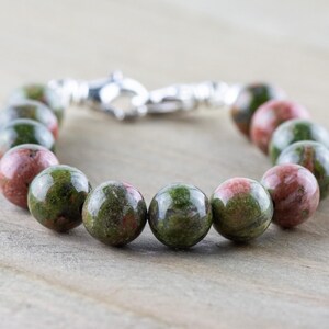 Puede incluir: Un brazalete de piedras preciosas verdes y rosas con cierre de plata. El brazalete est&aacute; hecho de cuentas redondas.