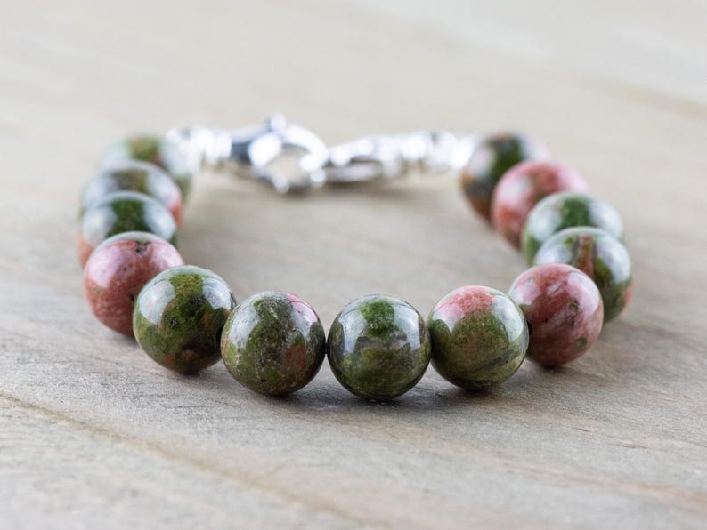 Puede incluir: Un brazalete de piedras preciosas verdes y rosas con cierre de plata. El brazalete est&aacute; hecho de cuentas redondas.