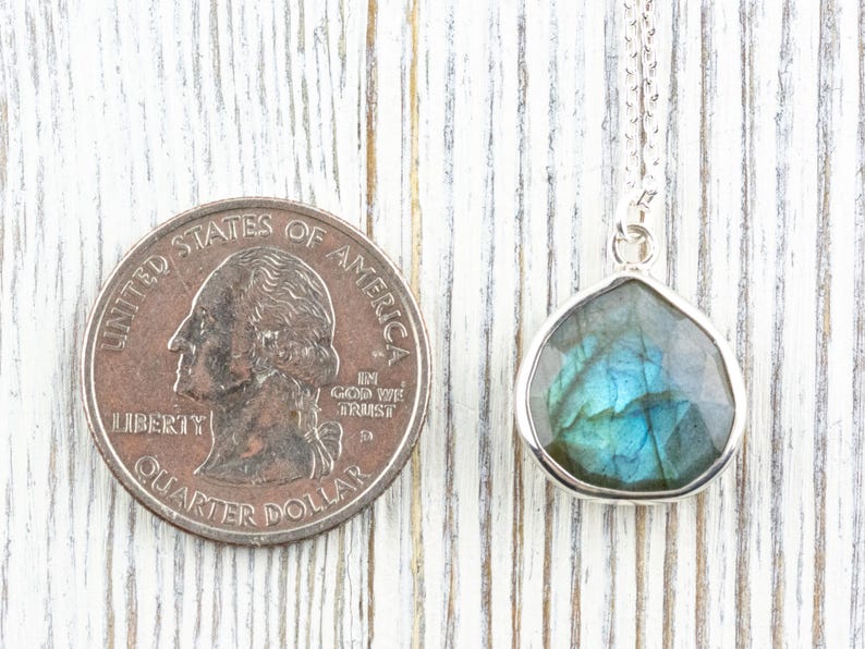 Pu&ograve; includere: Collana con pendente in argento con una pietra di labradorite sfaccettata a forma di goccia. La pietra mostra sfumature iridescenti blu e verdi. Una moneta da venticinque centesimi americana &egrave; accanto al pendente per il confronto delle dimensioni.