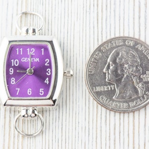 May include: A silver-toned watch with a purple face and white numbers. The watch is about the size of a UK 20 pence coin.