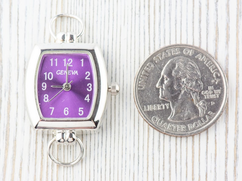 May include: A silver-toned watch with a purple face and white numbers. The watch is about the size of a UK 20 pence coin.