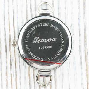 May include: The back of a silver watch with the text "STAINLESS STEEL BACK JAPAN MOV'T. WATER RESISTANT" and "Geneva 12495SB" engraved on it.