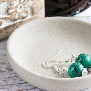May include: A pair of silver earrings with green malachite stone beads. The earrings are on a white ceramic dish.