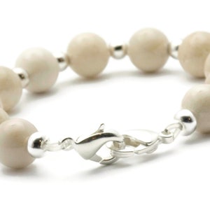 Op de afbeelding: Een witte kralen armband met een zilveren sluiting. De kralen zijn rond en hebben een licht getextureerd oppervlak.