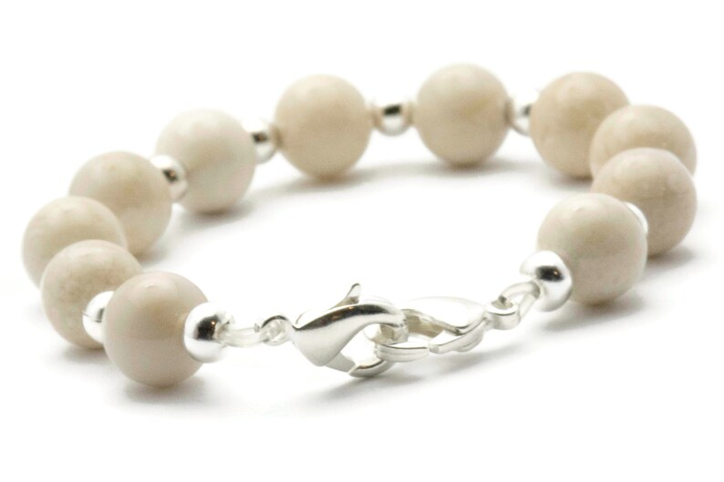 Op de afbeelding: Een witte kralen armband met een zilveren sluiting. De kralen zijn rond en hebben een licht getextureerd oppervlak.