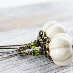 May include: A pair of dangle earrings with white and brown patterned beads, green crystal accents, and antique brass findings.