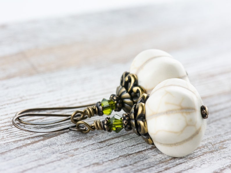 May include: A pair of dangle earrings with white and brown patterned beads, green crystal accents, and antique brass findings.