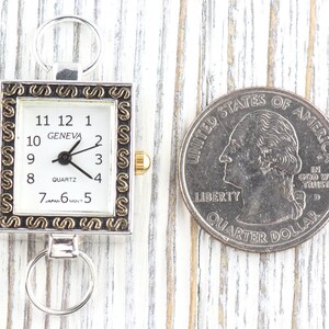 Peut inclure: Une montre Geneva &agrave; quartz rectangulaire avec un cadre argent&eacute; et un cadran blanc. La montre a des chiffres et des aiguilles noirs, avec une couronne dor&eacute;e. Une pi&egrave;ce de 25 cents am&eacute;ricaine est &agrave; c&ocirc;t&eacute; de la montre.