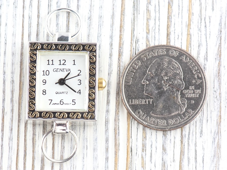 Peut inclure: Une montre Geneva &agrave; quartz rectangulaire avec un cadre argent&eacute; et un cadran blanc. La montre a des chiffres et des aiguilles noirs, avec une couronne dor&eacute;e. Une pi&egrave;ce de 25 cents am&eacute;ricaine est &agrave; c&ocirc;t&eacute; de la montre.