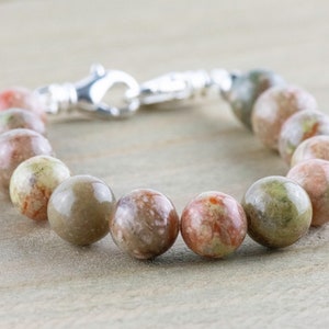 Pu&ograve; includere: Un braccialetto di perline con perline rotonde multicolori nei toni del verde, marrone e rosso. Il braccialetto ha una chiusura color argento. Le perline hanno un diametro di circa 2 cm.
