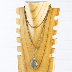 May include: A gold chain necklace with a turtle pendant on a wooden display stand. The turtle is made of metal and has a detailed design.