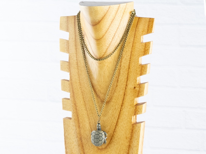 May include: A gold chain necklace with a turtle pendant on a wooden display stand. The turtle is made of metal and has a detailed design.
