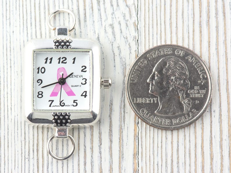 Pu&ograve; includere: Orologio quadrato color argento con quadrante bianco, numeri neri e design a nastro rosa. L'orologio &egrave; accanto a un quarto di dollaro USA. L'orologio ha un anello nella parte superiore e inferiore per il fissaggio.