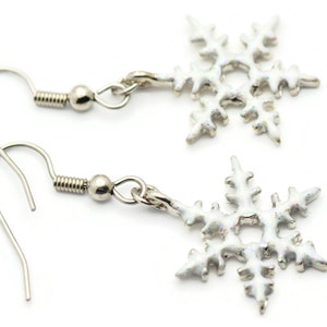 May include: A pair of silver snowflake earrings with white enamel. The earrings have a hook closure.