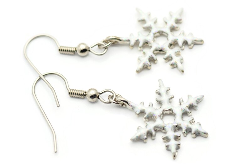 May include: A pair of silver snowflake earrings with white enamel. The earrings have a hook closure.