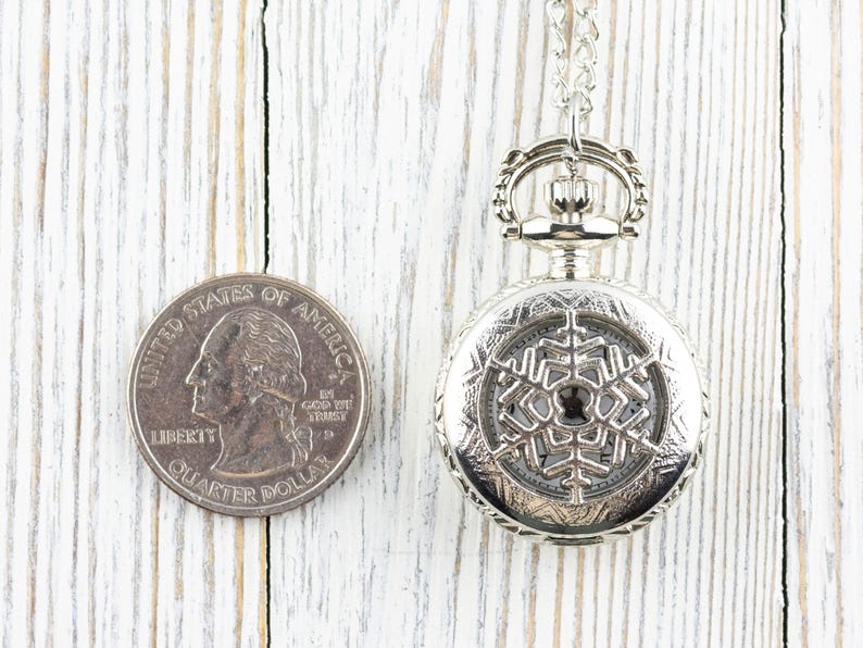 May include: A silver pocket watch with a snowflake design on the face. The watch is about the size of a UK 20 pence coin.