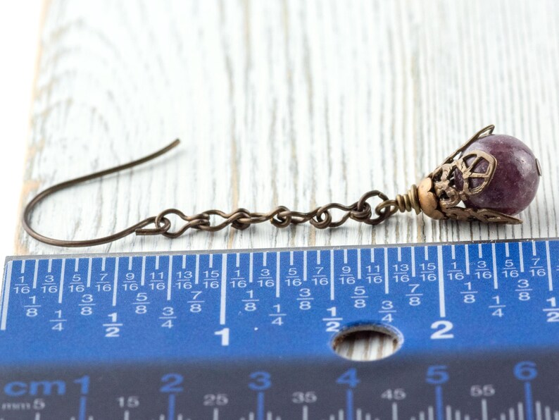May include: A single antique bronze earring with a purple gemstone bead. The earring features a decorative filigree cap and a chain link design. The earring is approximately 2.5 cm long, as shown by the ruler.