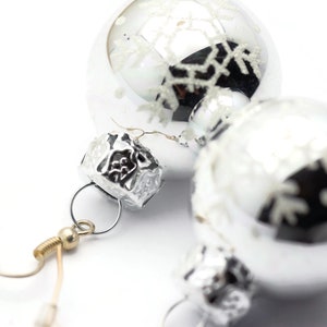 May include: Silver Christmas ornament earrings with snowflake designs. The earrings have a silver hook and a silver bead.