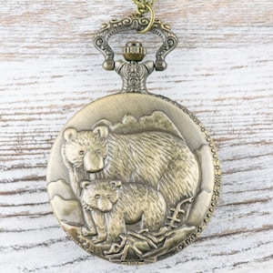 May include: A gold-toned pocket watch with a detailed design of a mother bear and her cub. The watch has a decorative chain attached.