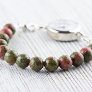 Puede incluir: Un reloj plateado con una pulsera de piedra moteada de verde y rojo.