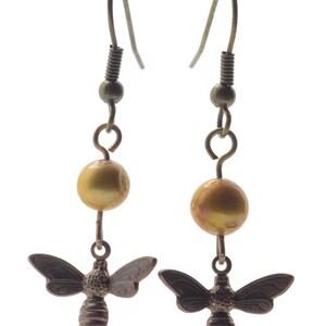 May include: A pair of gold tone earrings with a dangling bee charm and a gold pearl bead.