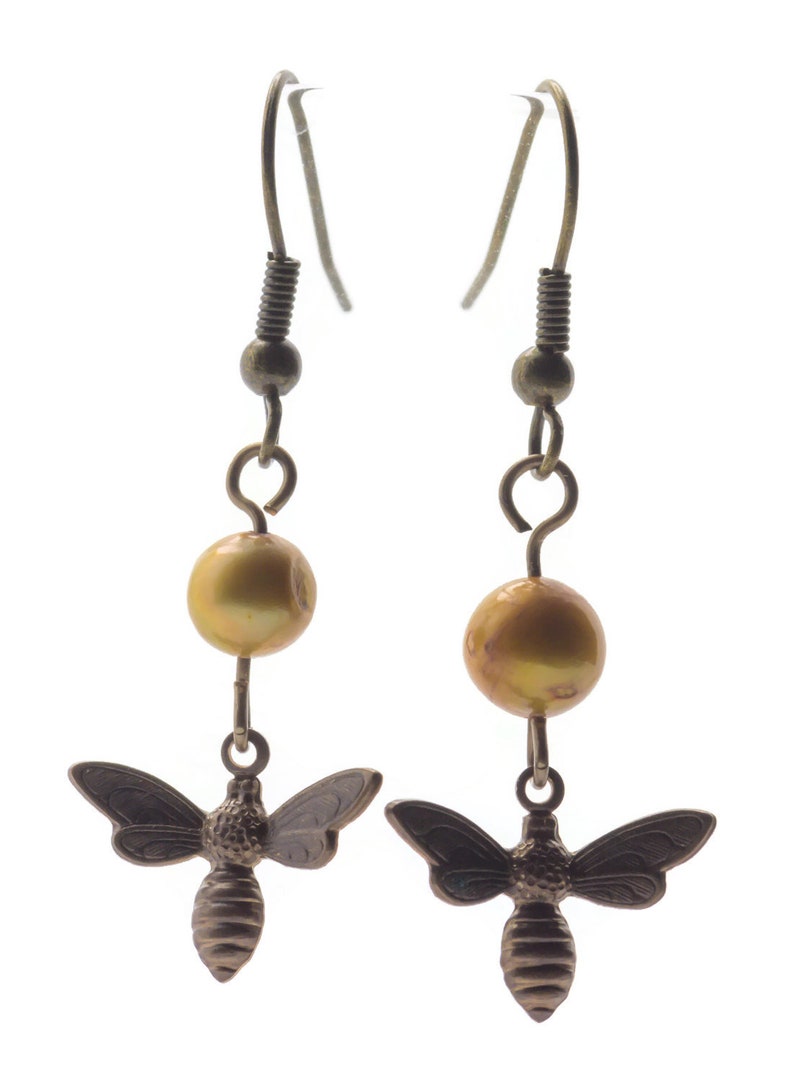 May include: A pair of gold tone earrings with a dangling bee charm and a gold pearl bead.