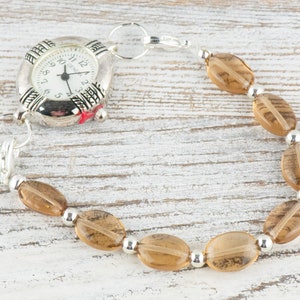 May include: A silver watch with a brown beaded bracelet. The watch face has black Roman numeral markings and a silver second hand.