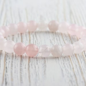May include: A pink rose quartz beaded bracelet with a light pink and white color gradient.