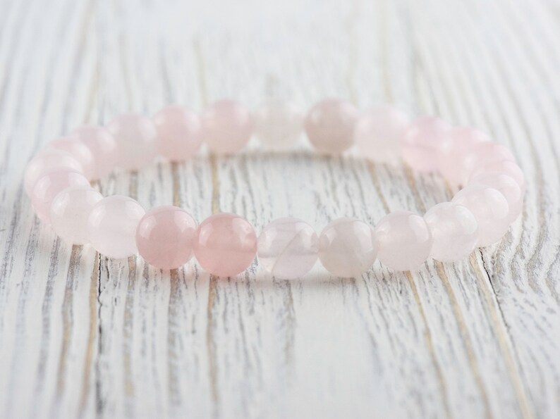 May include: A pink rose quartz beaded bracelet with a light pink and white color gradient.