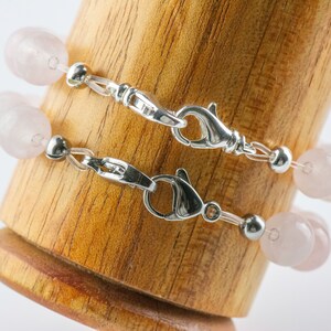 Puede incluir: Dos pulseras delicadas con cierres plateados y cuentas de color rosa p&aacute;lido. Las pulseras se muestran sobre una superficie de madera.