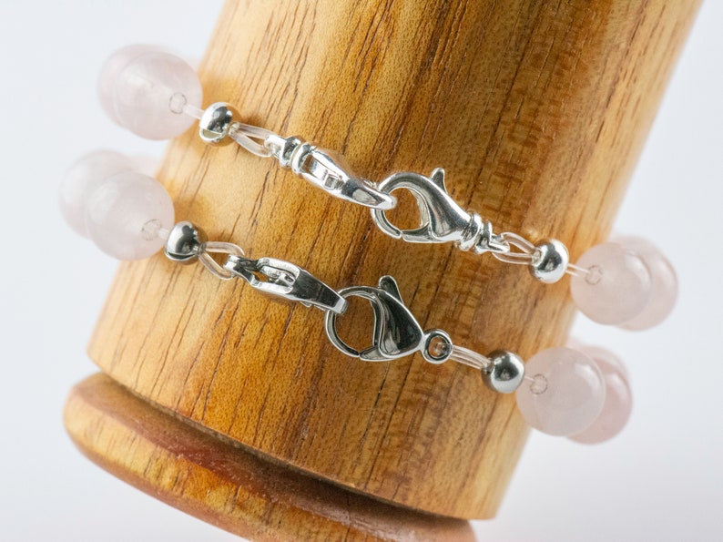 Puede incluir: Dos pulseras delicadas con cierres plateados y cuentas de color rosa p&aacute;lido. Las pulseras se muestran sobre una superficie de madera.