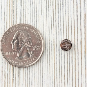 Pu&ograve; includere: Una moneta da un quarto di dollaro americano in argento e una batteria per orologio in argento si trovano su una superficie di legno bianco. La moneta presenta il profilo di George Washington e le parole "United States of America", "Liberty", "In God We Trust" e "Quarter Dollar". La batteria &egrave; etichettata con "SR626SW", "Maxell", "Hg 0" e "Japan".