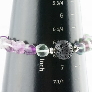 Puede incluir: Un brazalete de piedras preciosas de color morado, verde y blanco con una cuenta de lava negra y cuentas espaciadoras de plata. El brazalete mide 6,5 pulgadas de largo.
