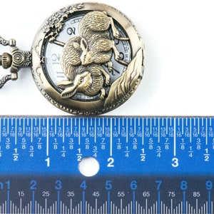 Puede incluir: Reloj de bolsillo antiguo de bronce con un relieve detallado de dos conejos. La esfera del reloj es blanca con n&uacute;meros y agujas negras. El reloj mide aproximadamente 5 cm de di&aacute;metro.