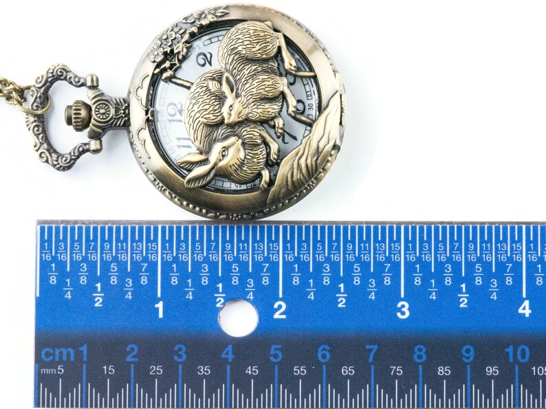 Puede incluir: Reloj de bolsillo antiguo de bronce con un relieve detallado de dos conejos. La esfera del reloj es blanca con n&uacute;meros y agujas negras. El reloj mide aproximadamente 5 cm de di&aacute;metro.