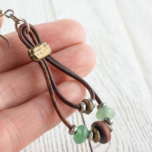 Pu&ograve; includere: Orecchini in pelle fatti a mano in stile boh&eacute;mien. Gli orecchini presentano cordoncini in pelle marrone, dettagli in ottone e una combinazione di perline verdi e marroni. Il design &egrave; a goccia, con chiusura a gancio. Sono leggeri.