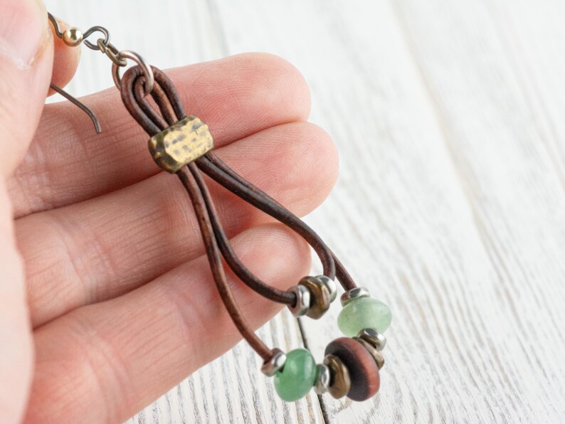 Pu&ograve; includere: Orecchini in pelle fatti a mano in stile boh&eacute;mien. Gli orecchini presentano cordoncini in pelle marrone, dettagli in ottone e una combinazione di perline verdi e marroni. Il design &egrave; a goccia, con chiusura a gancio. Sono leggeri.