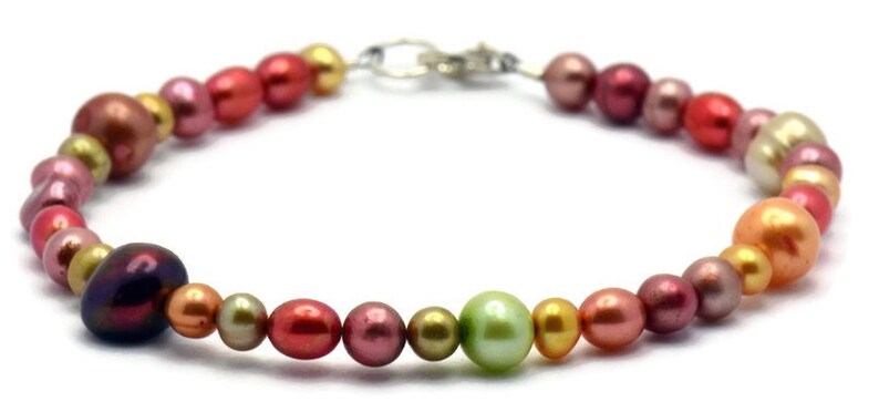 Pu&ograve; includere: Un braccialetto di perle multicolori con una chiusura argentata. Le perle sono in tonalit&agrave; di rosa, rosso, oro e verde.