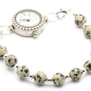 May include: A silver watch with a white face and black numbers is attached to a bracelet made of speckled brown and black beads.