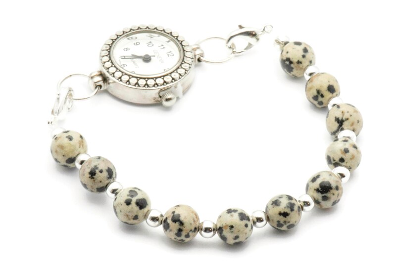 May include: A silver watch with a white face and black numbers is attached to a bracelet made of speckled brown and black beads.