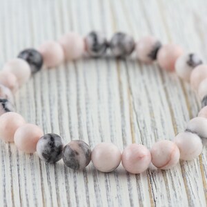 May include: A pink and gray gemstone bracelet with round beads. The bracelet is made of natural stones and is a beautiful and unique piece of jewelry.