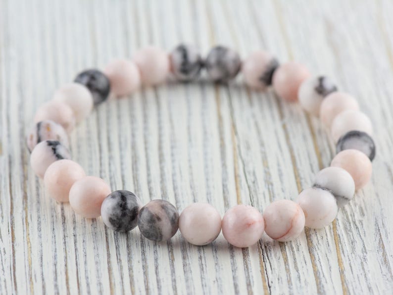 May include: A pink and gray gemstone bracelet with round beads. The bracelet is made of natural stones and is a beautiful and unique piece of jewelry.